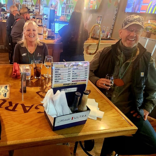 Two patrons smiling at a table in Brewgards Lounge, with drinks and a menu visible.