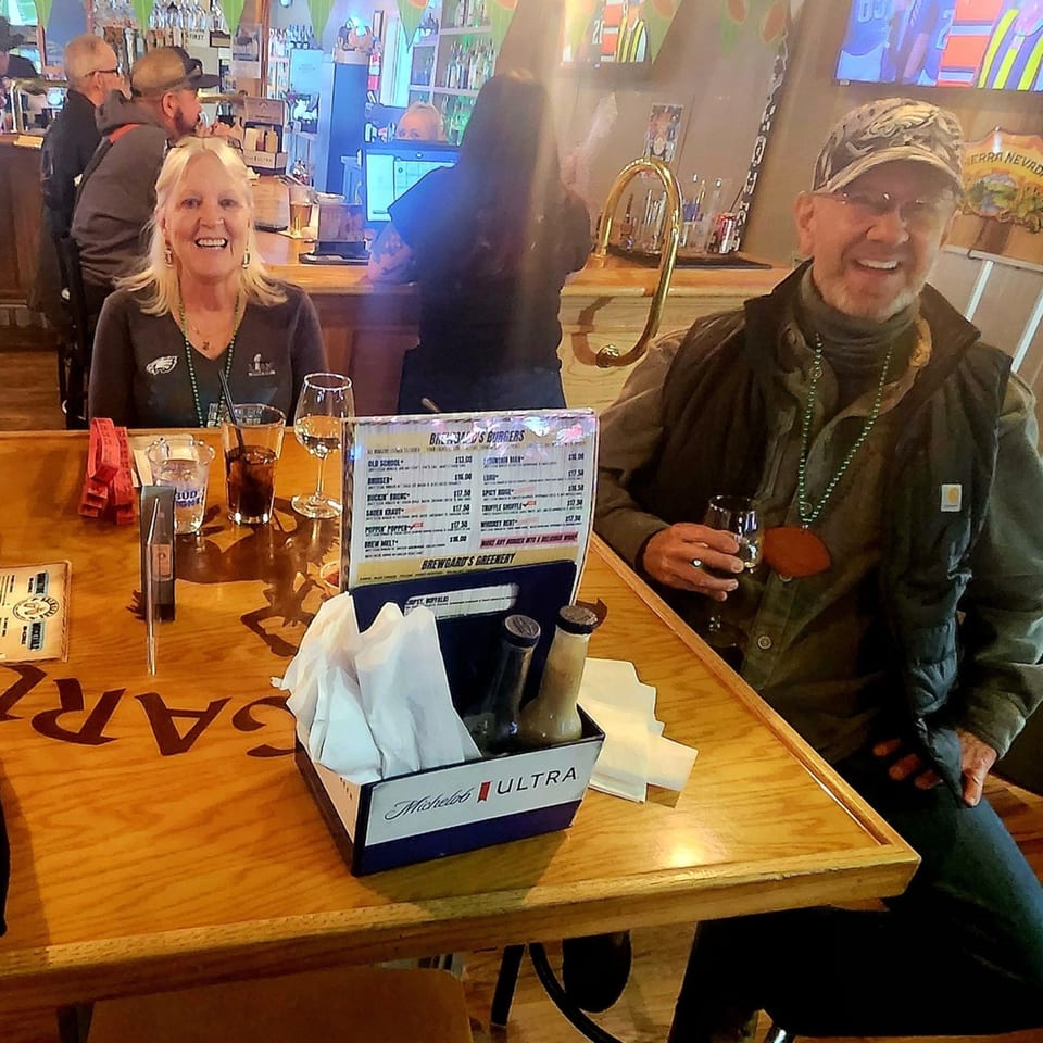 Two patrons smiling at a table in Brewgards Lounge, with drinks and a menu visible.