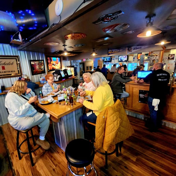 Patrons enjoying food and drinks at a bar-and-grill, with a bartender serving at the counter.