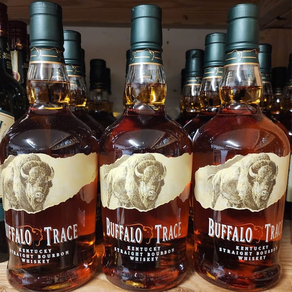 Rows of Buffalo Trace Kentucky Straight Bourbon Whiskey bottles with dark green caps on a wooden shelf.
