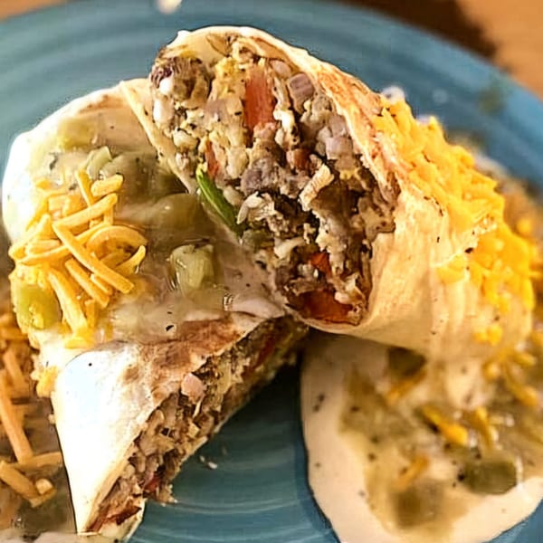 Two halves of a breakfast burrito filled with meat, eggs, and vegetables, topped with cheese.