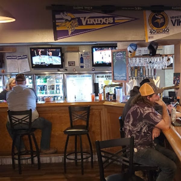Patrons seated at the wooden bar of Brewgards Lounge, with TVs, beer taps, and Vikings banners visible.