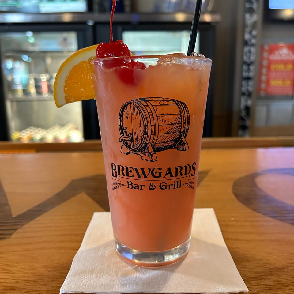 A Brewgards Bar & Grill cocktail, garnished with an orange slice and cherries, sits on a bar.