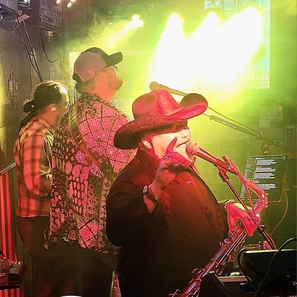 A band performs live at Brewgards Lounge, with a singer in a cowboy hat at the microphone.