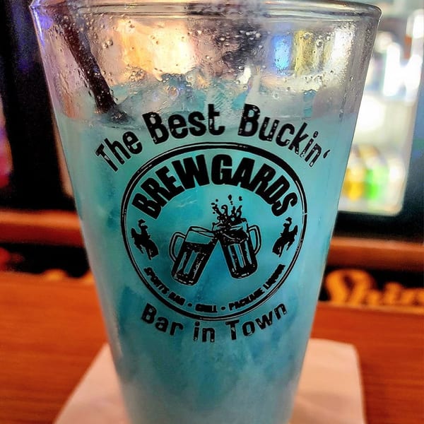 Close-up of a Brewgards Lounge glass with a blue drink and the bar's logo.