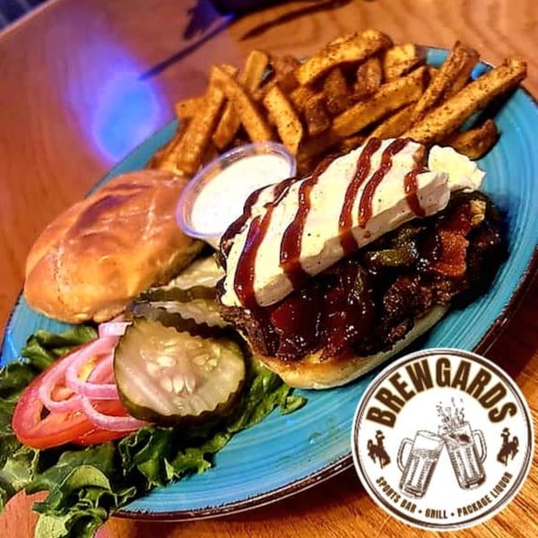 Brewgards Lounge's BBQ sandwich with fries, pickles, tomato, onion, and lettuce on a blue plate.