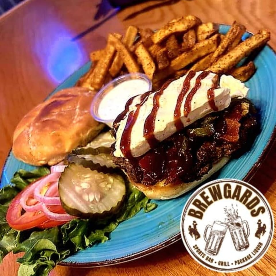 Brewgards Lounge's BBQ sandwich with fries, pickles, tomato, onion, and lettuce on a blue plate.