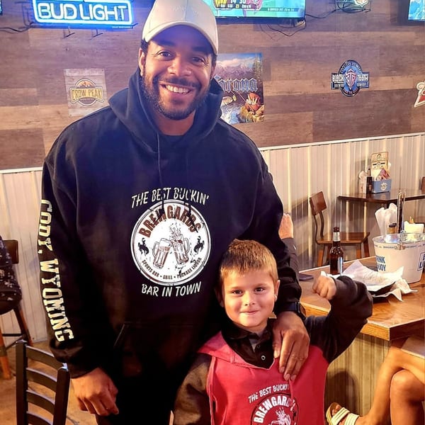 A man and a child smiling, wearing Brewgards Lounge hoodies, inside the bar-and-grill.