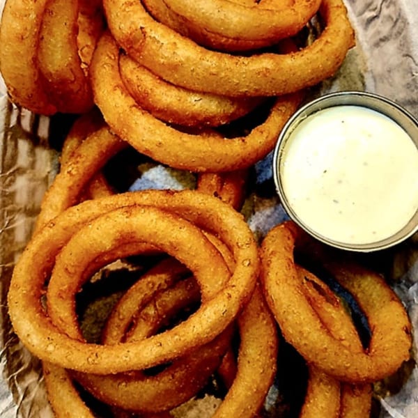 Golden-brown onion rings with a side of creamy dipping sauce on crinkled paper.