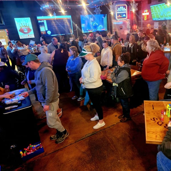 A crowded bar-and-grill with people standing and sitting, watching sports on multiple large screens.