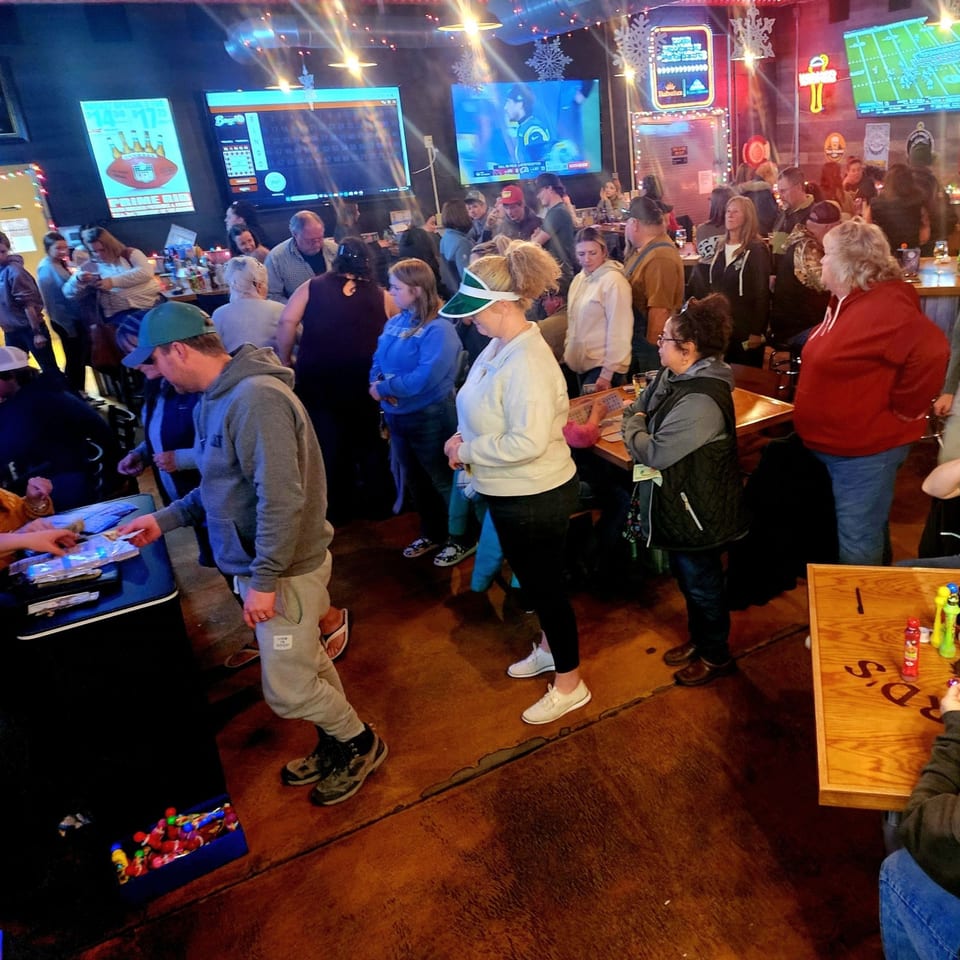A crowded bar-and-grill with people standing and sitting, watching sports on multiple large screens.